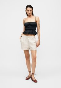 Μαύρο τοπ πεπλούμ με ρυθμιζόμενες λεπτές τιράντες, σετ με μπεζ λινά σορτς που διαθέτουν ελαστική μέση και κορδόνι. Καφέ επίπεδα δερμάτινα παπούτσια με κορδόνια.