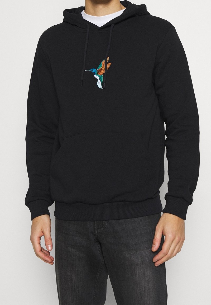 Schwarzer Hoodie mit einem bunten bestickten Kolibri-Design auf der Brust, ausgestattet mit einer Kängurutasche sowie gerippten Bündchen und Saum.