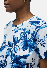Camiseta floral con un estampado botánico en azul y blanco, cuello redondo y mangas cortas. Tejido de algodón suave con costuras visibles.