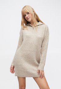 Rochie pulover bej cu textură striată, mâneci lungi și guler cu fermoar pe jumătate. Croială standard, lungime până la genunchi, concepută pentru confort.