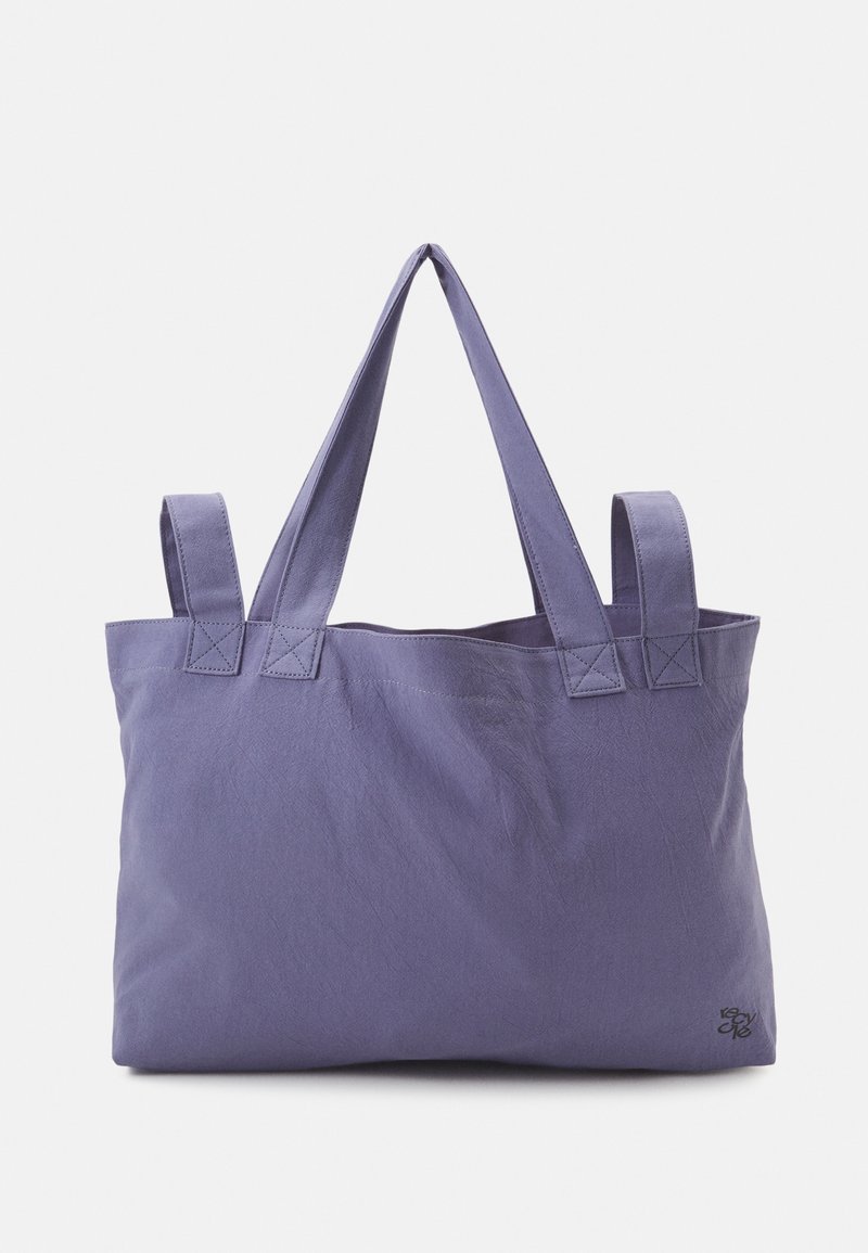 Sac fourre-tout en tissu violet avec deux larges sangles d'épaule, forme rectangulaire, texture douce et détails de couture aux attaches des sangles.