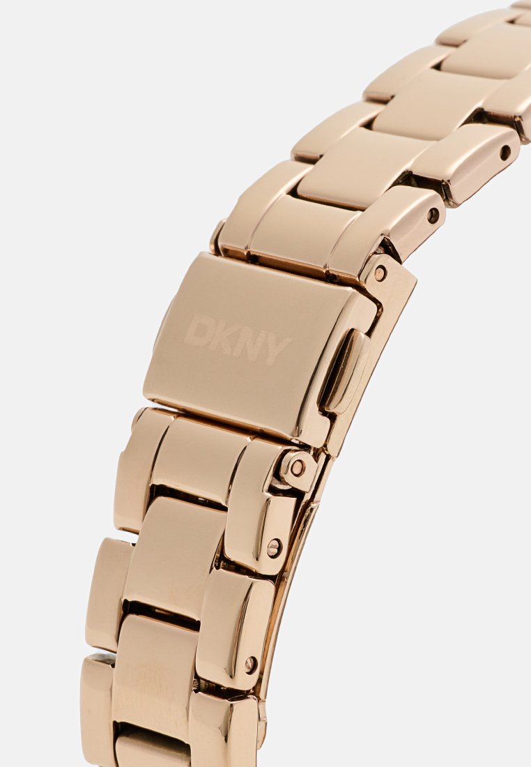 Bransoleta zegarka DKNY w różowym złocie, metalowa, z polerowanymi ogniwami, z zapięciem z wygrawerowanym logo oraz gładką, lustrzaną powierzchnią.