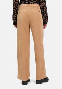 Beige corduroy broek met wijde pijpen en een geribbelde structuur, voorzien van twee achterzakken en gecombineerd met zwarte plateau schoenen.