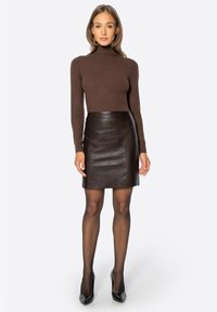 Top a collo alto in maglia marrone abbinato a una minigonna aderente in pelle marrone scuro. Modella con tacchi neri e calze nere trasparenti.