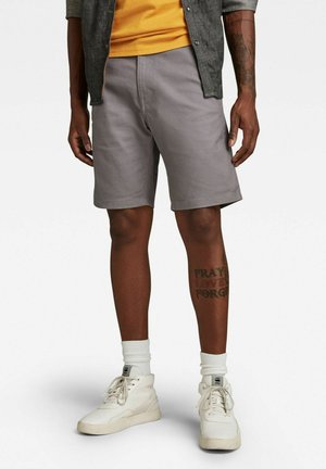 Pantaloni shorts grigi realizzati in tessuto di misto cotone, caratterizzati da una vestibilità slim, tasche frontali e orlo pulito. Indossati con scarpe sportive bianche alte e calzini leggeri.