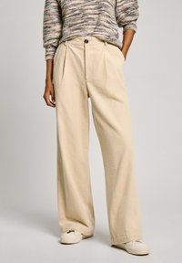 Beige wide-leg pants made of textured fabric, featuring a high waist and front pleats, paired with a multicolored knitted sweater.