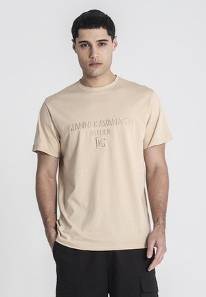 Camiseta de algodón beige de manga corta, con la marca en relieve "Gianni Kavanagh Atelier" en la parte frontal. Textura suave y diseño de cuello redondo.