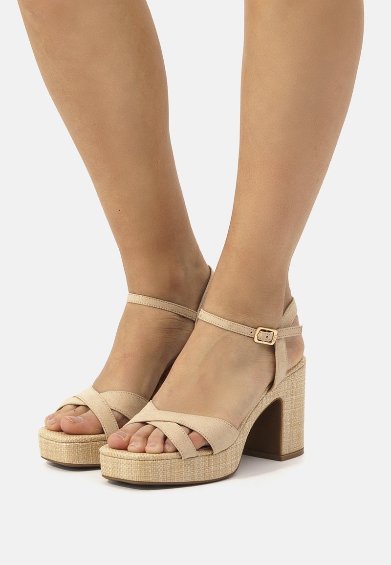 Sandali platform beige con cinturini incrociati, cinturino alla caviglia con fibbia e tacco intrecciato testurizzato. La soletta mostra le dita dei piedi scoperte.