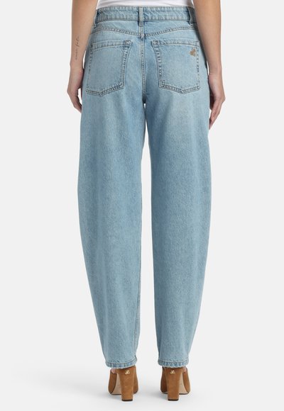 Svijetloplave široke hlače visokog struka s dva stražnja džepa, nošene s braon cipelama s blok petom na osobi koja stoji okrenuta leđima.