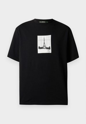 Camiseta negra de manga corta con un estampado rectangular blanco centrado de la Torre Eiffel y una firma debajo.