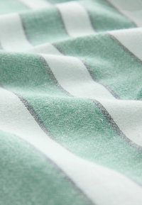 Tekstilmateriāls ar vertikālām svītrām zaļā un baltā krāsā, kam ir mīksta tekstūra un smalka austā raksts.