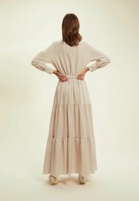 Robe maxi fluide à manches longues en tissu léger avec des rayures verticales pastel et un ourlet en étage, mettant en avant une taille ajustée et un col rond.