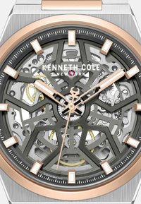 Zegarek skeleton z stalową kopertą, czarną tarczą, różowozłotymi akcentami i geometrycznymi wzorami. Posiada otwarte mechanizmy oraz luminescencyjne wskazówki.