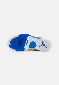 La semelle de la chaussure présente une base en caoutchouc blanc avec un motif en arêtes de poisson, des accents bleus et un logo Jumpman en bleu contrastant.
