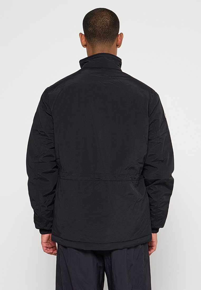 Giubbotto imbottito nero con colletto alto, cuciture visibili e vestibilità morbida. Presenta una vita arricciata e un tessuto testurizzato. Mostrata la vista posteriore.