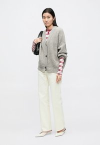 Gray oversized cardigan with ribbed texture, two buttons, worn over a red and white striped long-sleeve shirt, paired with cream pants and pointed shoes.
