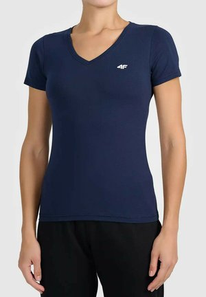 Vrouw draagt een aansluitend donkerblauw T-shirt met V-hals en korte mouwen met een wit "4F"-logo op de borst en zwarte broek.