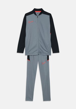 Ensemble de survêtement gris Nike comprenant une veste zippée avec des manches noires et des accents rouges, associée à un pantalon assorti avec des poches latérales.