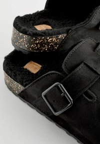 Crne suede sandale s teksturiranim crnim plišastim podstavom. Podesivi remen s crnom kopčom. Cork podnožje s točkom crne i zlatne boje.