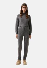 Grauer Strickpullover mit hohem Kragen, kombiniert mit passenden Jogginghosen mit Kordelzug und gerippten Bündchen. Tragen mit beigen Turnschuhen.