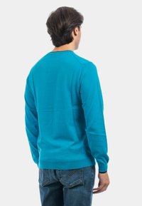 Maglione turchese a maglia con scollatura a girocollo e maniche lunghe. Texture liscia, design aderente e polsini e orlo a costine.