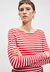 Červenobiely pruhovaný dlhý rukáv košeľa s lodičkovým výstrihom, vyrobená z jemného materiálu. Košeľa má priliehavé rukávy a voľný strih.