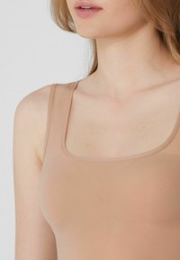Dámské tílko v barvě nude, se čtvercovým výstřihem a tenkými ramínky vyrobené z hladkého, elastického materiálu.