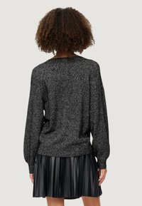 Maglione nero in tessuto testurizzato con una vestibilità ampia e maniche a palloncino, abbinato a una gonna nera in ecopelle plissettata. Entrambi gli indumenti sono privi di decorazioni.