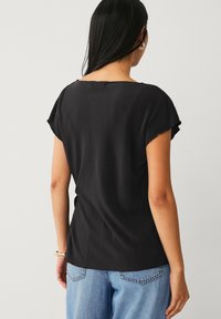 Sort plisseret top med korte ærmer, rund halsudskæring og afslappet pasform. Teksturområde med vandrette ribber. Kombineret med lyseblå jeans.