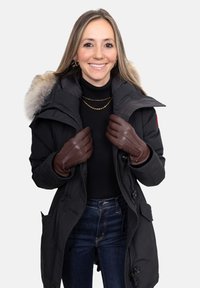 Black parka with fur-lined hood, layered over a black turtleneck. Brown leather gloves feature detailed stitching. Dark denim jeans complete the look.