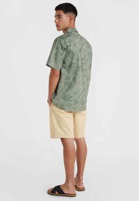 Kurzärmliges grünes Hemd mit Blumenmustern, kombiniert mit hellgelben Shorts. Verfügt über eine entspannte Passform und eine Gesäßtasche für zusätzlichen Komfort.