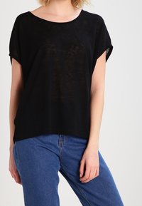 Černý krátký rukáv top s širokým výstřihem, vyrobený z lehké, mírně průhledné látky, spárován s modrými džíny s vysokým pasem.