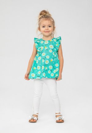 Haut sans manches turquoise avec imprimé floral blanc et jaune, épaules froncées, assorti à un legging blanc et des sandales décoratives.
