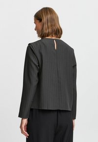 Blazer nero rigato con scollatura rotonda, maniche lunghe e dettaglio a chiave sul retro, realizzato in tessuto morbido. Vestibilità tailored.