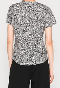 Top a maniche corte con un motivo floreale in bianco e nero, scollatura rotonda e orlo leggermente curvo. Realizzato in tessuto leggero.