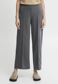 Sive široke hlače z mehko teksturo, s visokim pasom in dvema navpičnima šivoma spredaj. Obute so v bež udobne čevlje.