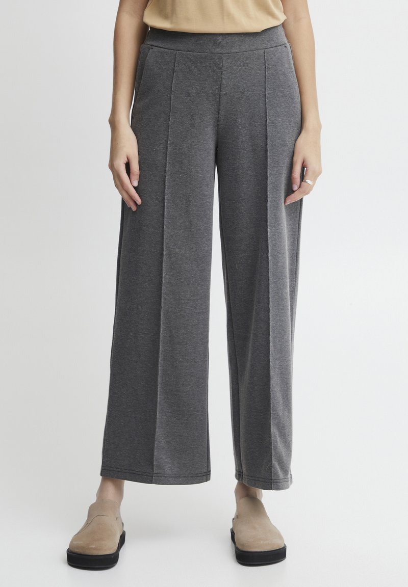 Sive široke hlače z mehko teksturo, s visokim pasom in dvema navpičnima šivoma spredaj. Obute so v bež udobne čevlje.