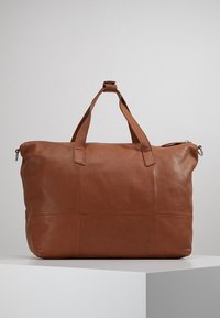 Bolso tote de cuero marrón con asas dobles, cierre de cremallera y textura suave. Presenta una forma rectangular simple con detalles de costura.