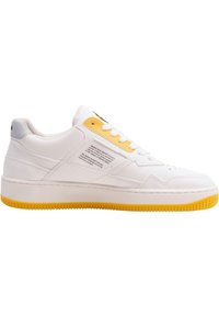 White sneakers with yellow accents, textured leather upper, round toe, flat sole, and branding on the side. Features lace-up front.