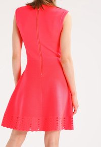 Robe ajustée rose avec un tissu texturé, design sans manches et fermeture éclair au dos. Présente un ourlet festonné avec des découpes.