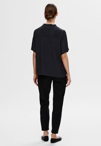Schwarzes T-Shirt mit kurzen Ärmeln, vertikalen Streifen, geradem Schnitt und Rückenpasse, kombiniert mit schwarzen, schmal geschnittenen Hosen und schwarzen Ballerinas.
