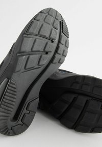 Black athletic shoes with textured rubber soles, featuring a cushioned midsole and smooth accents. The design emphasizes durability and grip.