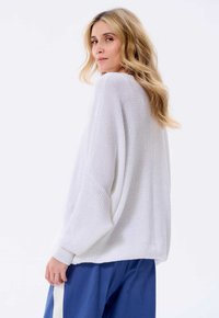 Witte gebreide trui met een losse pasvorm, voorzien van verlaagde schouders en geribde manchetten, gecombineerd met blauwe broek. Zachte textuur en ademend materiaal.
