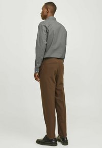 Chemise à motif gris avec un col, associée à un pantalon marron et des chaussures noires, vue de dos. Comprend des poignets à boutons et des poches latérales.