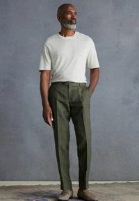 Light gray knit short-sleeve shirt paired with olive green tailored trousers, featuring a subtle texture, and beige loafers with minimal detail.