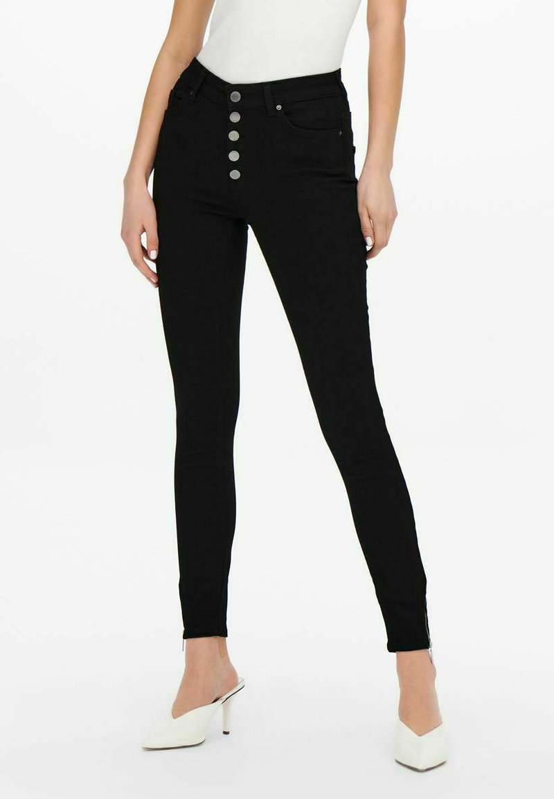Jeans skinny de tiro alto en negro con cierre de cinco botones, cremalleras laterales en los tobillos y una textura de denim suave y elástica.