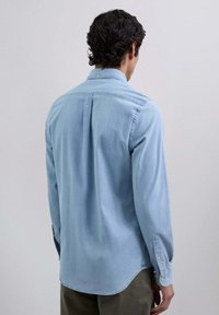 Lichtblauw, langemouwen shirt gemaakt van een zachte stof, met een geknoopte kraag, een ronde zoom en knoopaccenten op de manchetten.