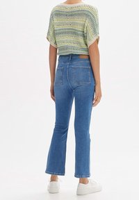 Top de punto a rayas verdes y azules con corte holgado, combinado con jeans de mezclilla azul de tiro medio y botines blancos.