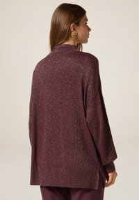 Bordowy sweter o luźnym kroju, teksturowana tkanina z srebrnym połyskiem, wysoki dekolt i boczne rozcięcia. Elegancki i prosty design.