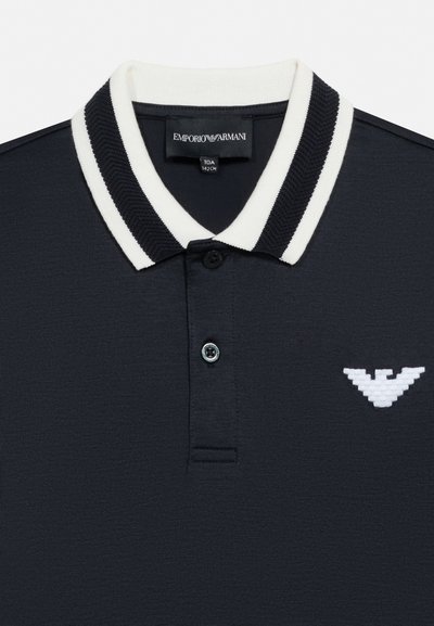 Mornarsko modra polo majica s črno-belim črtastim ovratnikom, dvema gumboma na sprednji strani in belim logotipom orla Emporio Armani na prsih.